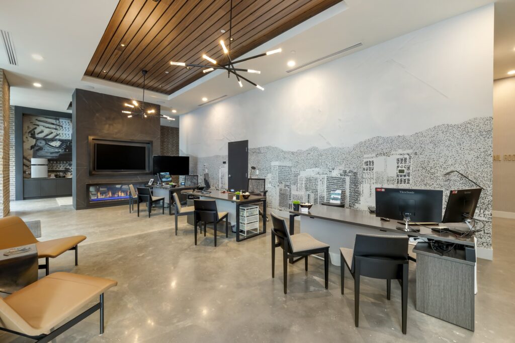 Modern office with multiple workstations, computers, chairs, a large mural on the wall, a fireplace, and polished concrete floors.