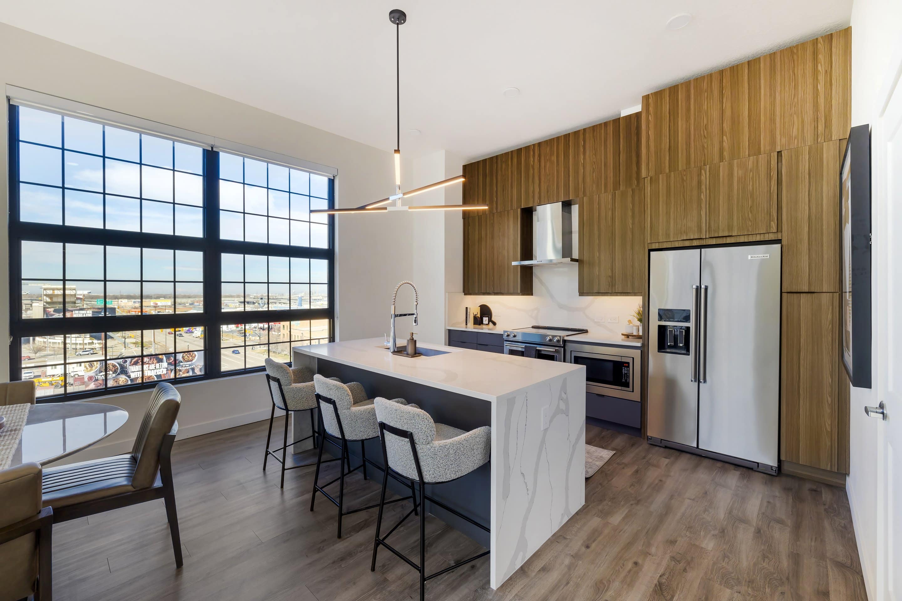 Modern kitchen with wood cabinets, stainless steel appliances, marble island with barstools, a large window, and a dining area overlooking Lake Cameron and boasting top-notch amenities.